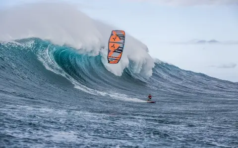 Ein Kitesurfer reitet eine riesige Welle bei Jaws, Hawaii. Die Welle bricht mit gewaltiger Kraft, während der Surfer mit seinem Kite in der Luft schwebt.