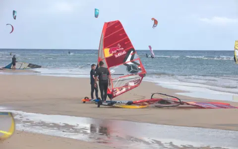 Windsurfer bereiten sich am Strand von Pozo Izquierdo, Gran Canaria, auf das Wasser vor. Mehrere bunte Segel und Boards liegen am Sand.