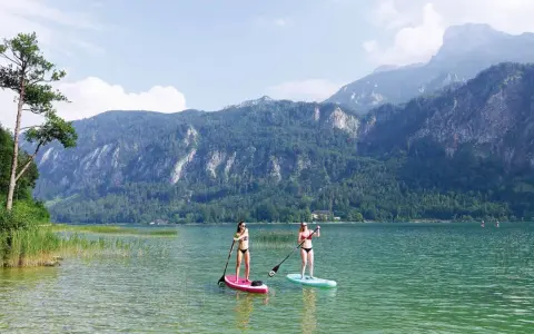 Zwei Frauen genießen Stand-Up-Paddling auf einem ruhigen See vor einer Bergkulisse. Perfekte sup spots für einen entspannten Tag.