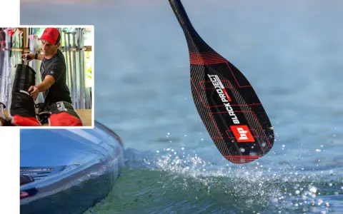 Mann bereitet sich auf ein sup fest vor. Ein Paddel mit schwarzem Carbonmuster und roten Akzenten taucht ins Wasser.