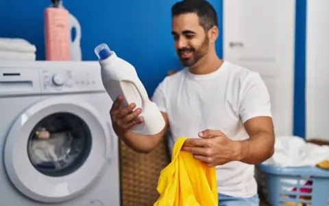 Mann hält Waschmittel und gelbes Trikot bereit, um die Wäsche zu waschen.