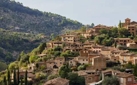 Mallorquinisches Dorf mit Steinhäusern und Terrassen an einem bewaldeten Hang.