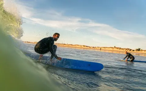 Surfer reitet eine Welle vor der Küste von Tarifa. Ein weiterer Surfer wartet im Wasser.