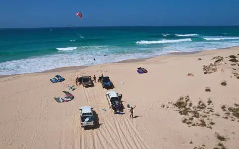 Kitesurfer bereiten sich auf das Windsurfen auf den Kapverden vor. Mehrere Kites liegen am Strand neben Autos.