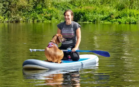 Frau und ihr sup hund krallen auf dem Fluss.
