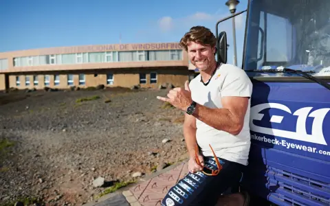 Bekannte deutsche Windsurfer: Ein Mann mit Sonnenbrille und Shaka-Geste lehnt an einem blauen Bus vor dem Centro Internacional de Windsurfing.