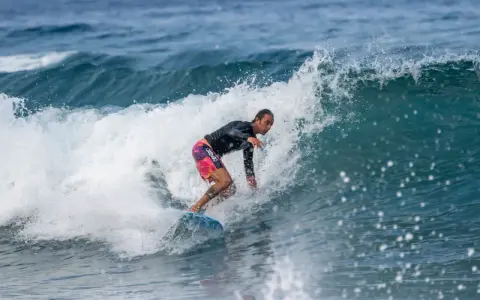 Ein Surfer reitet eine Welle vor Zypern. Er trägt ein schwarzes Rashguard und bunte Boardshorts.