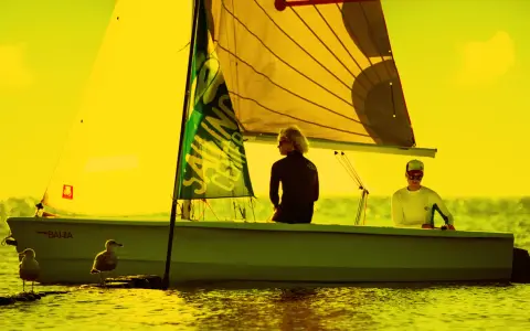 Zwei Segler auf einem Boot vor Hiddensee, bereit für Surf und Segel. Möwen beobachten das Geschehen.