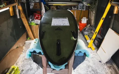 Surfboard liegt auf Ständer, bereit für die **Surfboard Reparatur**. Werkzeuge und Materialien im Hintergrund.