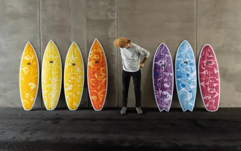 Mann mit Hut steht vor bunten Surfbrettern, bereit für das Wellenreiten.