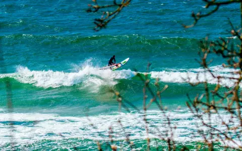 Windsurfer auf einer Welle vor Bornholm. Das türkisfarbene Meer und die Gischt erzeugen ein dynamisches Bild vom Surfen.