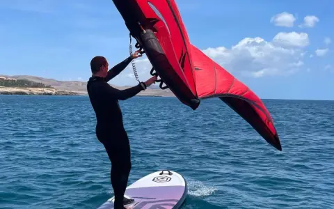 Mann mit rotem Wingboard auf dem Wasser vor Costa Calma. Perfekter Tag für Wassersport am Ion Club.