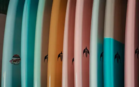 Reihe bunter Surfboards in Pastelltönen. Welches Surfboard passt zu mir? Die Auswahl ist groß, von hellblau bis rosa.