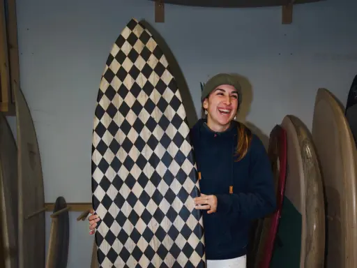 Frau lacht und hält ein selbstgebautes Surfbrett mit Rautenmuster.