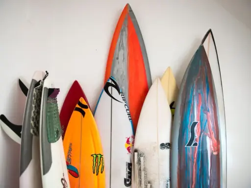 Eine Sammlung bunter Surfbretter steht an einer weißen Wand. Sie sind bereit für das nächste Abenteuer auf den Wellen beim Wellenreiten.