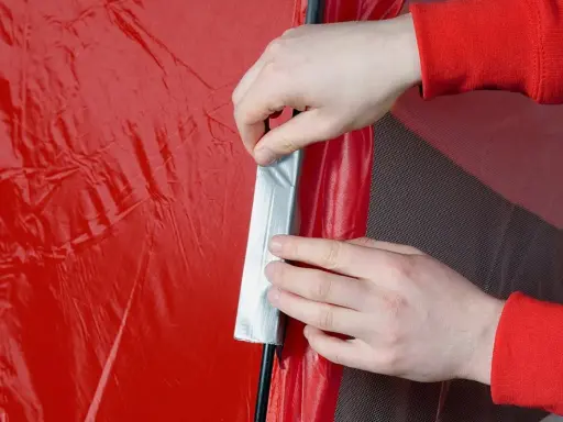 Hände flicken ein rotes Zelt mit silbernem Klebeband.