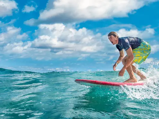 Ein Surfer reitet eine Welle vor der Küste der Dominikanischen Republik. Der Mann trägt ein blaues Shirt und bunte Badeshorts.
