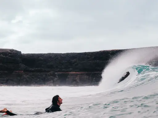 Surfer wartet auf die perfekte Welle vor der Felsküste. Windsurfen Fuerteventura.