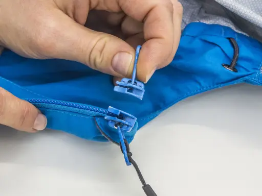 Hände tauschen den blauen Reißverschluss-Zipper an einer Jacke aus.