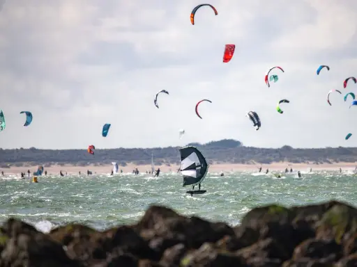 Viele bunte Kites und Surfer bevölkern das Meer am Brouwersdam Zeeland. Ein Kitefoiler schwebt über dem Wasser.