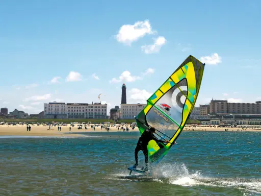 Windsurfer auf dem Meer vor Borkum, im Hintergrund der Strand mit Menschen und Hotels.