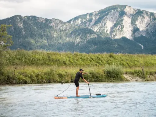 Mann auf SUP-Board, der geradeaus fährt, mit Bergen im Hintergrund.