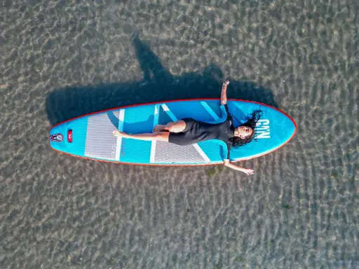 Frauen entspannt auf einem SUP-Board in NRW liegend. Das Board ist blau mit roten Akzenten.