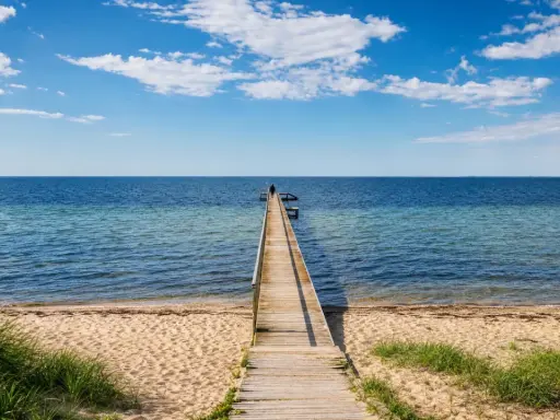 Holzsteg führt ins Meer am Ringkøbing Fjord. Eine Person steht am Ende des Stegs. Blauer Himmel mit Wolken.