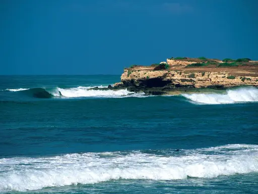 Türkisblaue Wellen brechen sich an einer felsigen Küste. Ein perfekter Tag für capo mannu surf.
