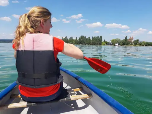 Frau paddelt im Kanu auf einem See, genießt sup touren deutschland. Im Hintergrund: Ufer mit Bäumen und Häusern.