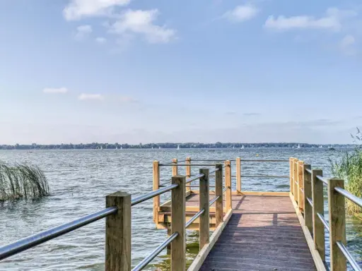 Holzsteg am Zwischenahner Meer mit Segelbooten am Horizont und Schilf am Ufer.