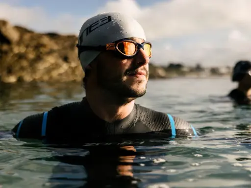 Mann mit Schwimmbrille und Badekappe im Wasser, bereit für das Schwimmen. Die Schwimmbrille reinigen ist wichtig für klare Sicht.