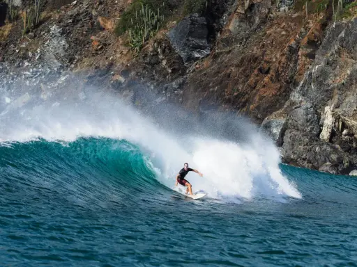 Surfer reitet eine grüne Welle vor einer felsigen Küste. Perfekt für die Surf-App, um die nächste Session zu planen.