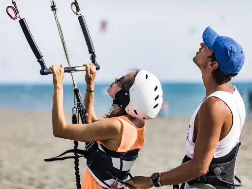 Frau und Mann bereiten sich auf das Surfen mit Drachen in der Hand vor. Sie stehen am Strand, das Meer im Hintergrund.