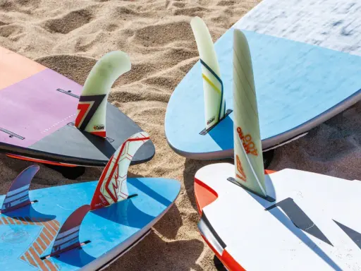Mehrere Windsurfboards mit bunten Finnen liegen im Sand. Perfekt, wenn Sie ein Windsurfboard kaufen möchten.