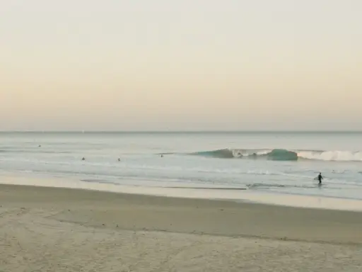 Ein Surfer geht ins Meer, um Cornwall zu surfen. Sanfte Wellen brechen am Strand.