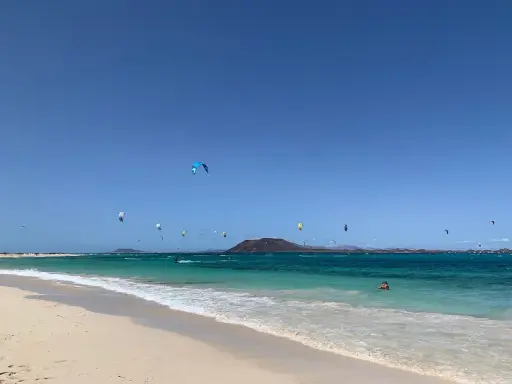 Kitesurfer tanzen über das türkisfarbene Wasser am Flag Beach Corralejo. Ein einsamer Schwimmer genießt die Sonne.