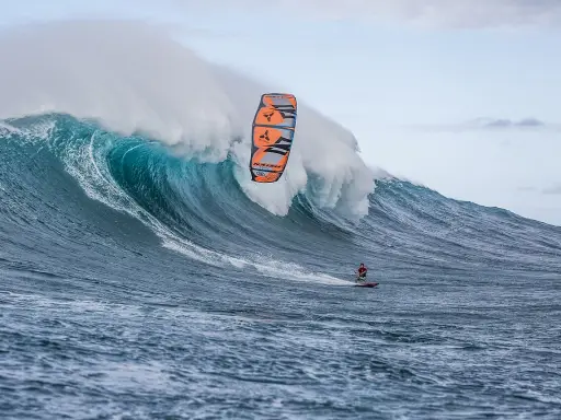 Ein Kitesurfer reitet eine riesige Welle bei Jaws, Hawaii. Die Welle bricht mit gewaltiger Kraft, während der Surfer mit seinem Kite in der Luft schwebt.
