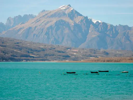 Boote treiben auf dem türkisfarbenen Lago di Santa Croce vor einer majestätischen Bergkulisse.