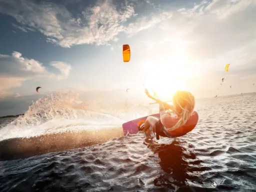 Kitesurferin genießt das Rhodos Surfen im goldenen Abendlicht, spritzt Wasser auf.