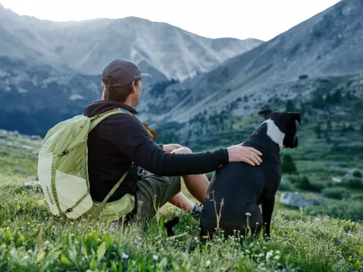 Mann mit Hund und Rucksack in den Bergen. Nach einer Wanderung ist der Rucksack reinigen eine gute Idee, bevor es weitergeht.
