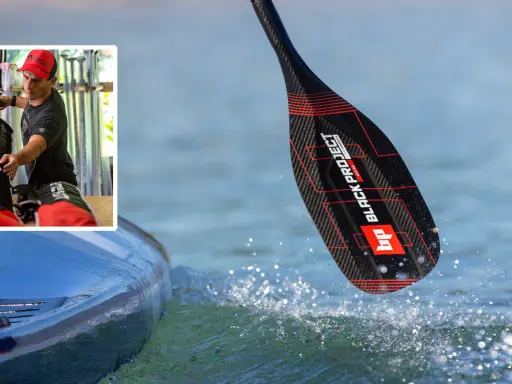 Mann bereitet sich auf ein sup fest vor. Ein Paddel mit schwarzem Carbonmuster und roten Akzenten taucht ins Wasser.