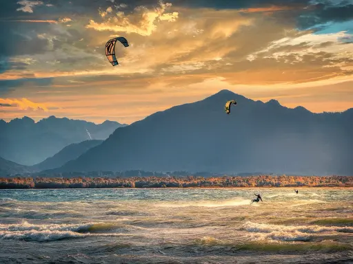 Kitesurfer gleiten über die Wellen am Chiemsee, während die Sonne hinter den Bergen untergeht. Ein traumhafter Abend für Windsurfen.
