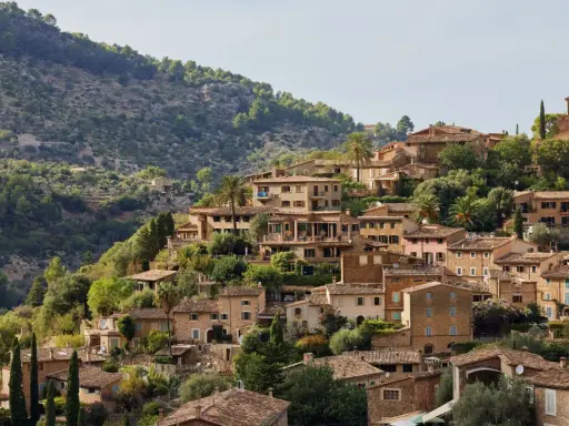 Mallorquinisches Dorf mit Steinhäusern und Terrassen an einem bewaldeten Hang.