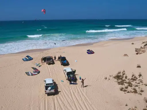 Kitesurfer bereiten sich auf das Windsurfen auf den Kapverden vor. Mehrere Kites liegen am Strand neben Autos.
