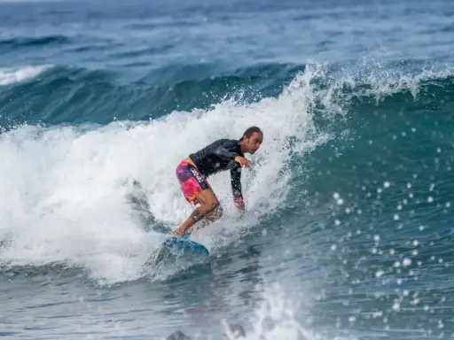 Ein Surfer reitet eine Welle vor Zypern. Er trägt ein schwarzes Rashguard und bunte Boardshorts.