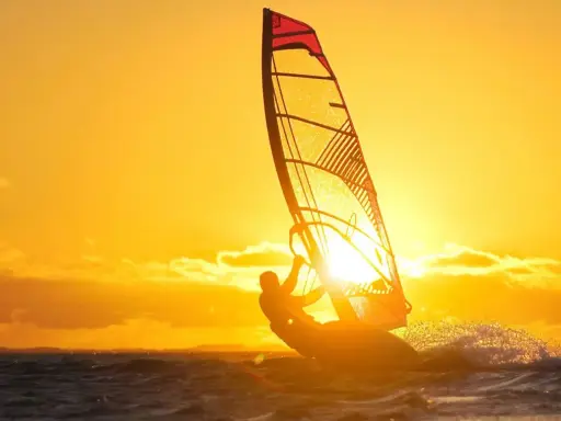 Ein Windsurfer genießt die untergehende Sonne am Ammersee. Das goldene Licht taucht die Szene in warme Farben.