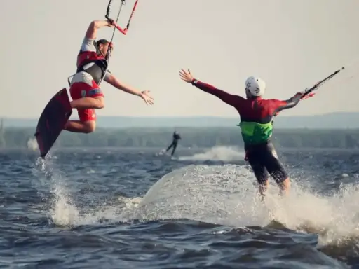 Zwei Kitesurfer springen und reichen sich die Hände auf dem Steinhuder Meer. Ein weiterer Surfer im Hintergrund.
