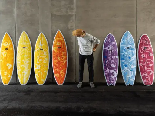 Mann mit Hut steht vor bunten Surfbrettern, bereit für das Wellenreiten.