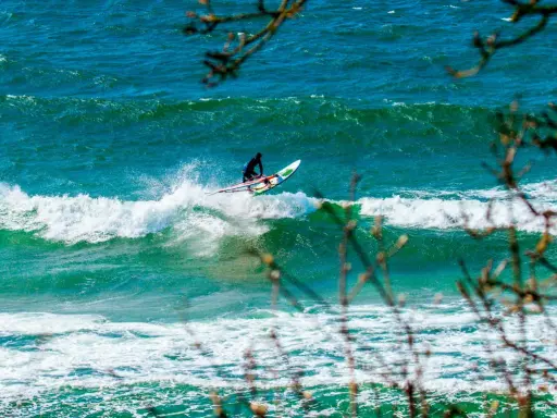 Windsurfer auf einer Welle vor Bornholm. Das türkisfarbene Meer und die Gischt erzeugen ein dynamisches Bild vom Surfen.